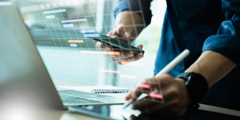 Close-up of a person's hands holding a phone and stylus near a laptop, overlaid with a digital project timeline or Gantt chart graphic.
