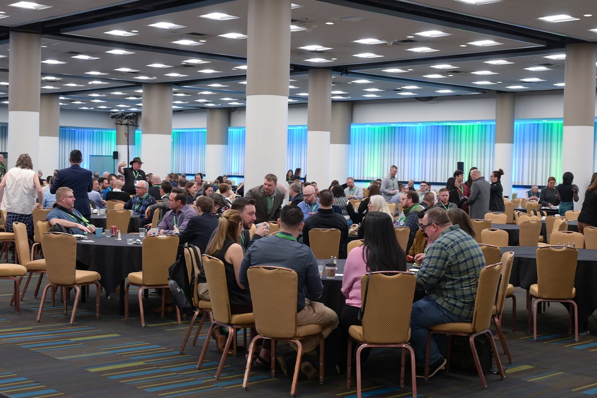 Attendees seated at round tables in conference hall with blue-lit windows