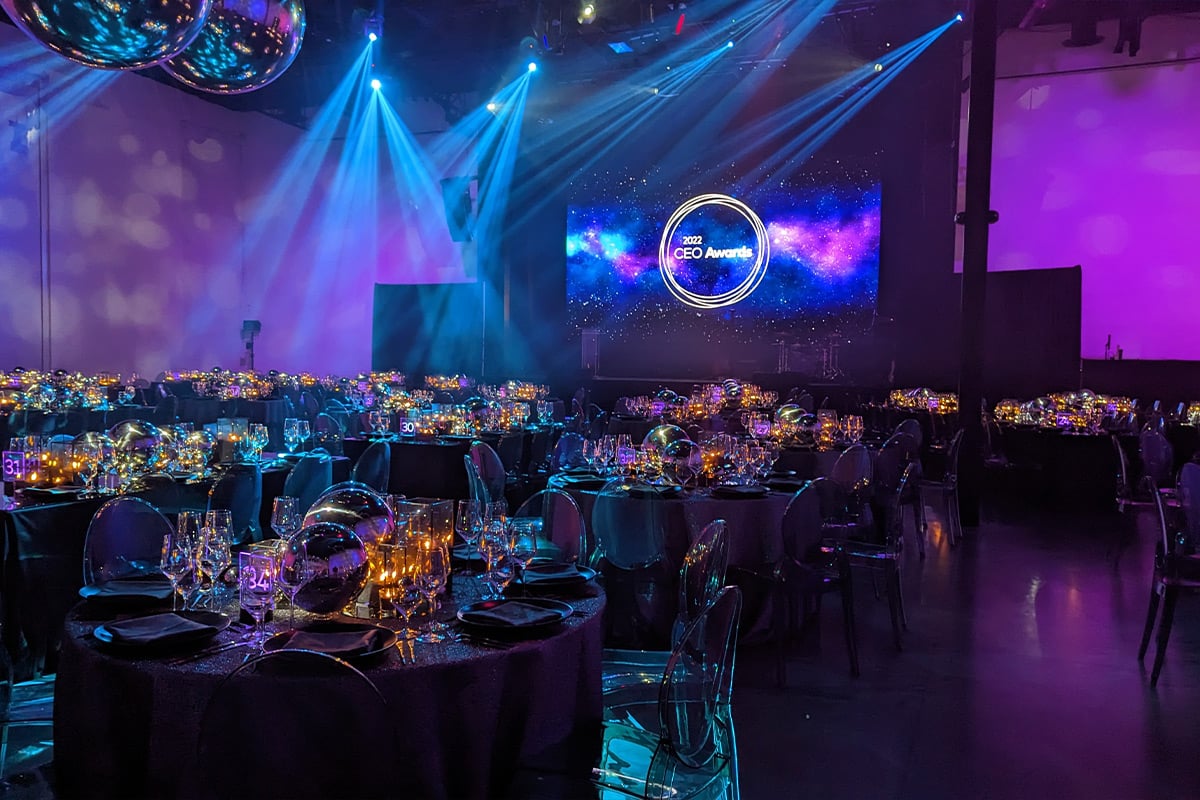 Elegant ballroom with dramatic blue lighting, disco ball, and formal dining tables set for awards ceremony.