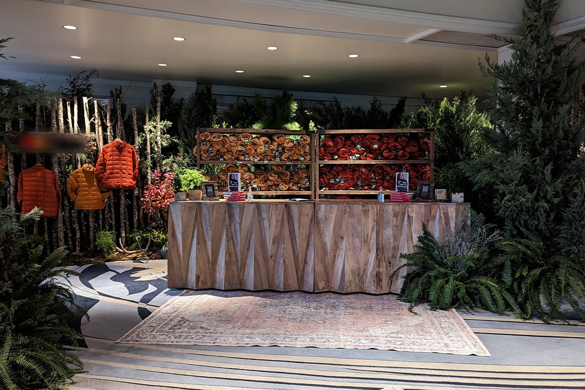 Rustic wooden retail counter displaying orange jackets on birch branch wall with forest-themed greenery.