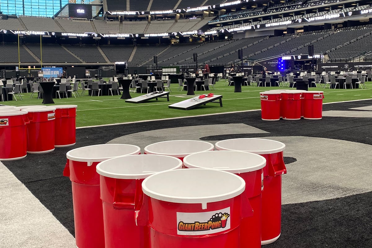 Giant beer pong setup on football field with stadium seating in background
