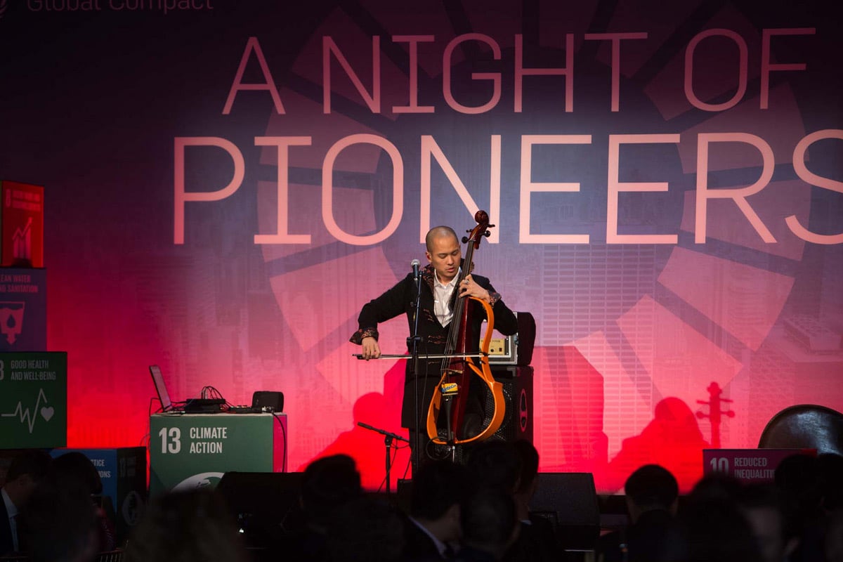 Cellist performs on stage under dramatic red lighting with "A Night of Pioneers" text displayed behind.