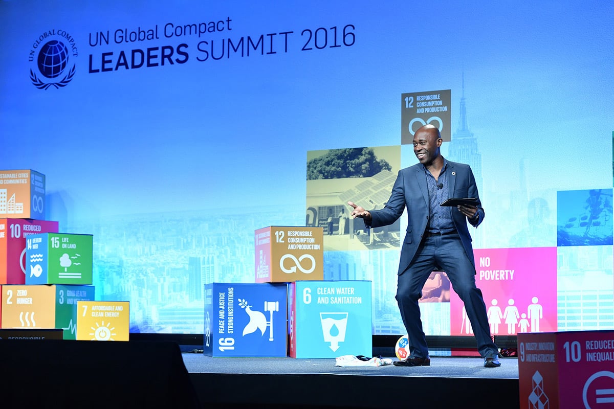 Speaker presents at UN Global Compact Leaders Summit 2016 surrounded by colorful sustainable development goal displays.