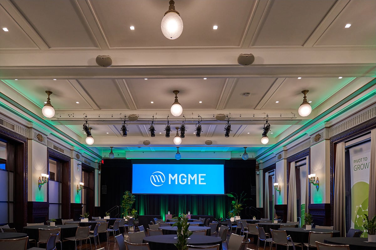 Elegant ballroom setup with MGME branding on screen and green stage lighting