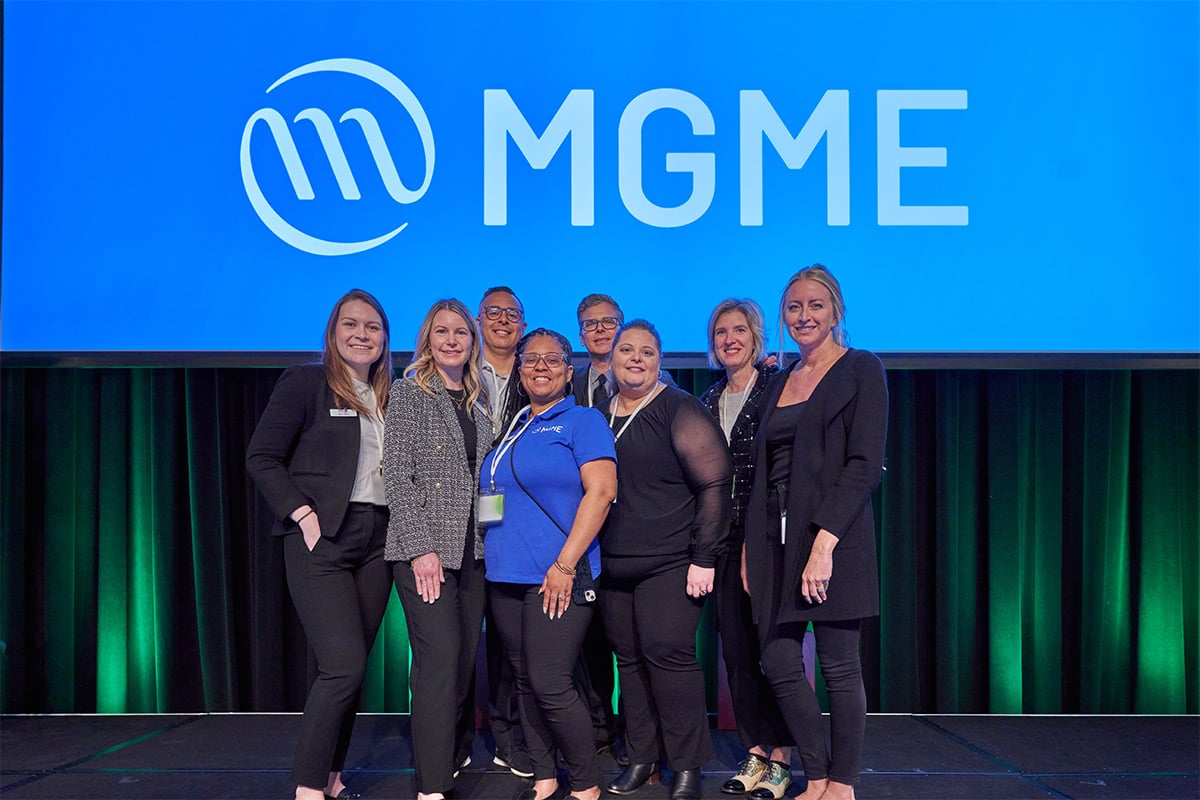 Group of eight women posing on stage in front of large MGME logo