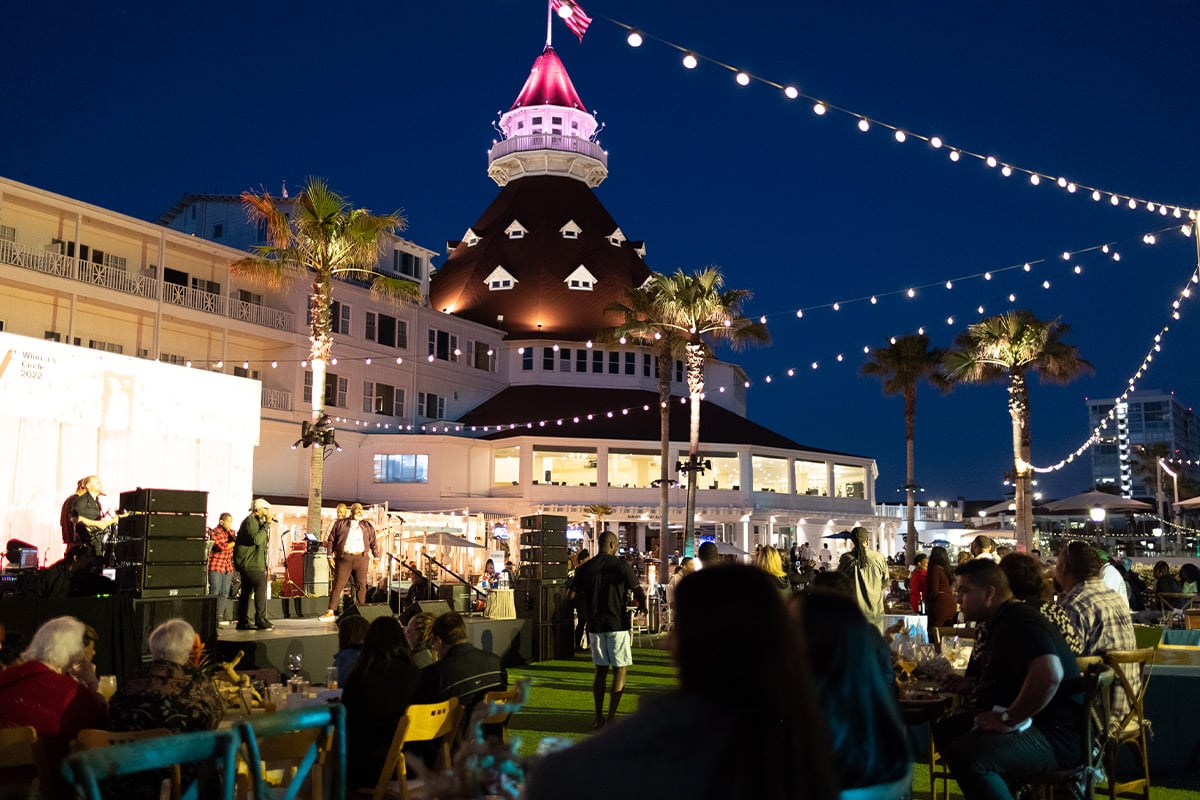 Evening event with historic hotel tower, palm trees, and string lights as crowd watches performance