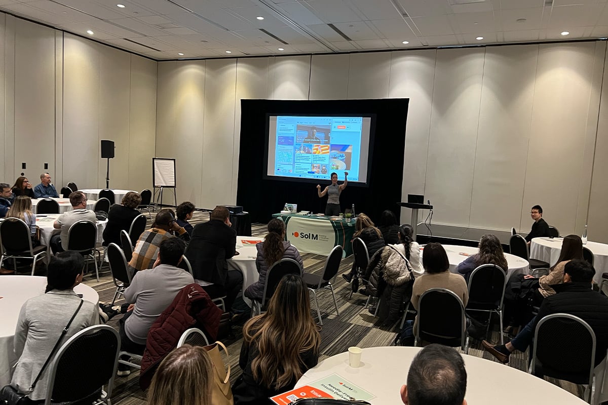 Presenter giving talk to seated audience in conference room with projection screen